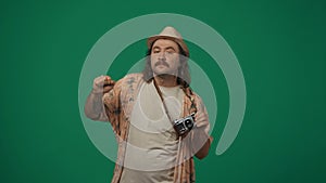 Man traveller in casual clothing and straw hat with old film cam over neck posing with funny moves. Isolated on green