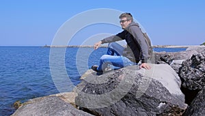 Man traveller comes at seashore sits huge stones admires seascape on vacation.