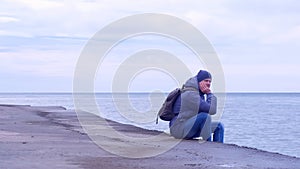 Man traveller sits on old waterfront at sea in winter day and looks at seascape.