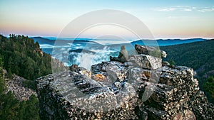 Man traveller sitting on rock at mountain top and meeting sunrise, heavy mist in deep valley.