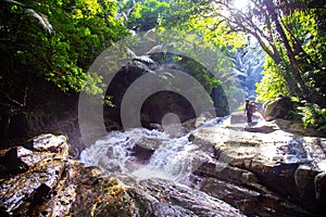 A man trekking in the tropical forest, with sunlight and waterfall