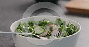 Man tries fresh salad with radish, cucumber and herbs in white bowl