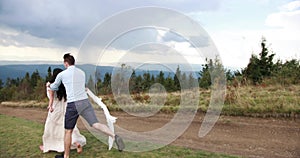 Man tries to catch smiling woman in lomg white dress while she runs away in the mountains