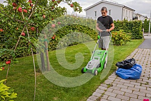 Man trimming green grass lawn with electric lawn mower.