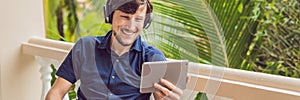 Man in tropics talking with friends and family on video call using a tablet and wireless headphones BANNER, long format