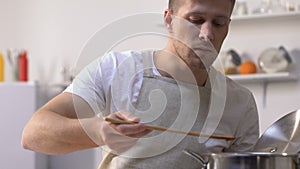 Man trying sauce in pan and screwing up face because of bad taste, cooking