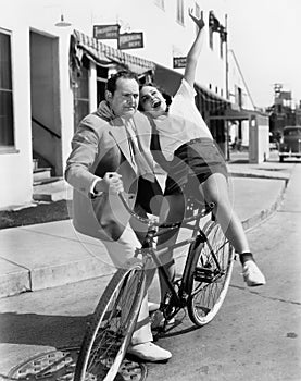 Man trying to balance an exuberant woman on a bicycle