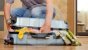 A man trying to pack overfilled suitcase