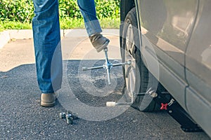 A man trying to twist off the bolt by his foot  using cross wrench for changing punctured wheel. Hole in the tire. Concept.
