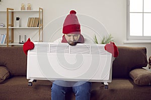 Man trying to warm up with an electric heater when it& x27;s very cold in the house in winter