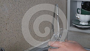 Man turn the knob to open the water, fill a glass with tap water, close-up. Water is quickly poured into an empty glass