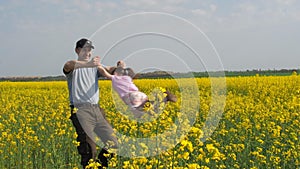 A man is turning a child. Dad turns his daughter in yellow. A happy family. Rapeseed field.