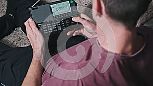 Man Turning Modern Portable Radio With Digital LCD Frequency Scale on Home Couch