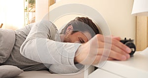 Man turning off alarm and going back to sleep