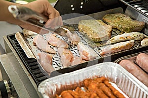 Man turning and roasting chicken filet, pork neck steaks, raw fresh sausages and marinated bacon wrapped skewers on gas grill BBQ