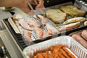 Man turning and roasting chicken filet, pork neck steaks, raw fresh sausages and marinated bacon wrapped skewers on gas grill BBQ