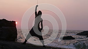 Man turns fire poi standing on a cliff near the ocean at sunset