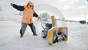 Man turns on a snow thrower in winter in an orange jacket