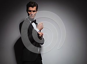 Man in tuxedo arranging his sleeve looks back over shoulder