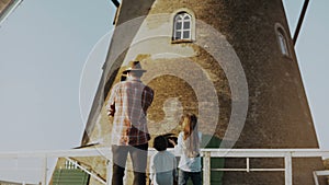 Man with two children near a rustic windmill. Dad with little kids shoots a live video on his smartphone. Back view. 4K.