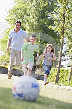 Man and two young children outdoors playing soccer