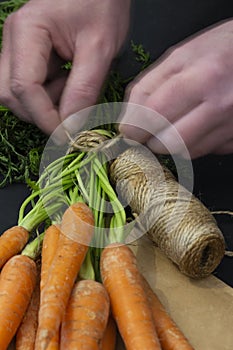 Man tying a bundle of carrots with garden string on a brown paper bag.