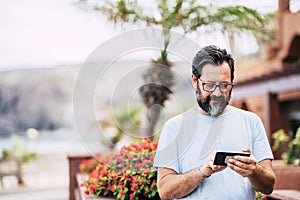 Man type on a modern cellular phone device in outdoor leisure activity with technology - portrait of aged adult with defocused