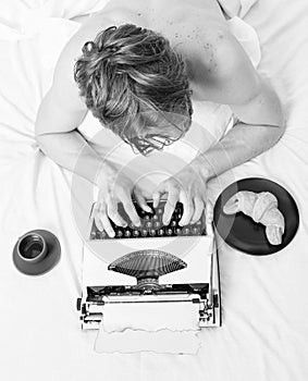 Man with typewriter and coffee lay bed. Author guy tousled hair busy write chapter deadline coming top view. Man