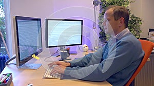 Man typing behind a computer with two screens