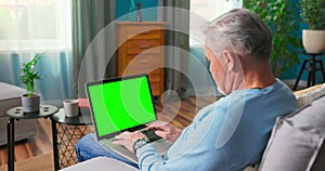 Man Typing on keyboard on Green Mock-up Screen Laptop Computer Sitting on a Couch at