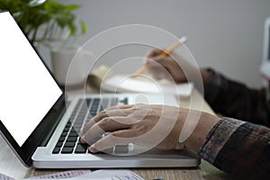 Man typing on keyboard pf computer laptop and making note on notepad.