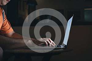 Man typing on keyboard and working at computer laptop in night