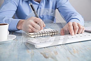 Man typing in keyboard and writing on notepad