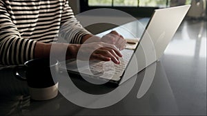 Man typing on a laptop at a table with wood flooring