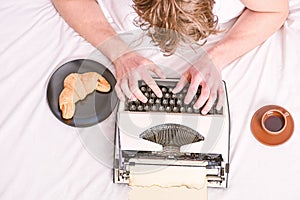 Man typing retro writing machine. Old typewriter on bedclothes. Male hands type story or report using vintage typewriter