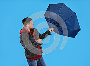 Man with umbrella caught in gust of wind on light blue background