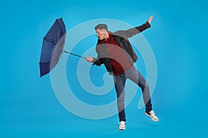 Man with umbrella caught in gust of wind on light blue background