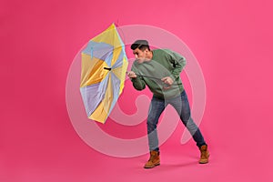 Man with umbrella caught in gust of wind on pink background