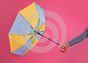 Man with umbrella caught in gust of wind on pink background, closeup