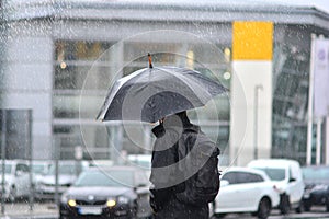 A man with an umbrella in the rain crossing the road.