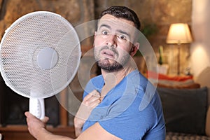 Man during unbearable heatwave using electric fan