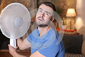 Man during unbearable heatwave using electric fan