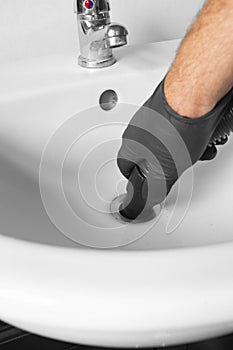 Man unblocking pipes in a bathroom sink using a hoover.