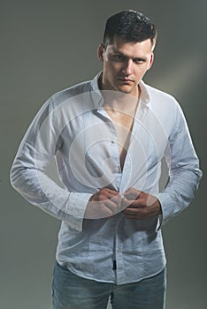 Man unbutton fashionable shirt. Young macho undress white shirt. Guy with serious face. model with elegant casual photo