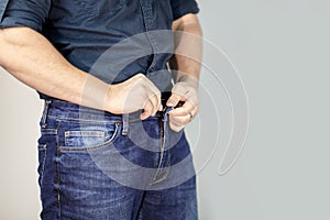 Man unbuttones blue jeans. Man torso, fingerring, blue shirt, casual wear.