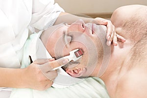 Man undergoes the procedure of medical micro needle therapy with a modern medical instrument derma roller.