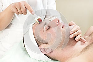 Man undergoes the procedure of medical micro needle therapy with a modern medical instrument derma roller.