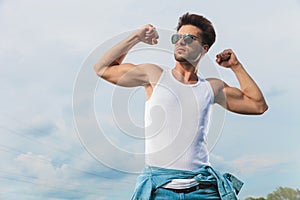 man in undershirt flexing his biceps outside
