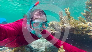 Man in an underwater mask is snorkeling in clear water. Underwater scene diver near rock of corals in Indian ocean.