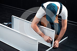 A man in uniform is assembling a white metal shelving in a room decorated with ebony